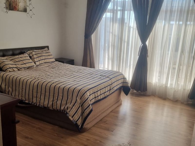 A bedroom featuring laminate flooring and large windows with curtain treatments, offering a functional and neutral space.