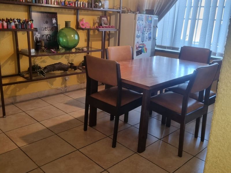 A dining area featuring ceramic floor tiles, a pendant light fixture, and vertical window blinds, providing a functional space for meals.