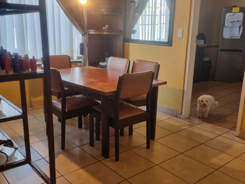 A dining area featuring ceramic tiled flooring, a built-in corner shelving unit, and a wall-mounted mirror, with an adjacent view into the kitchen area.