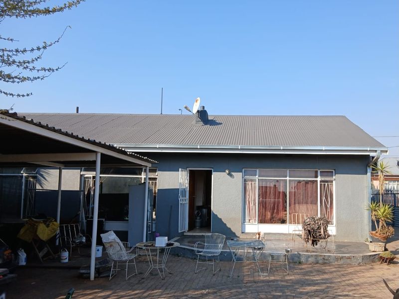 Rear view of the property featuring a paved patio area, corrugated metal roof, and a covered carport structure.