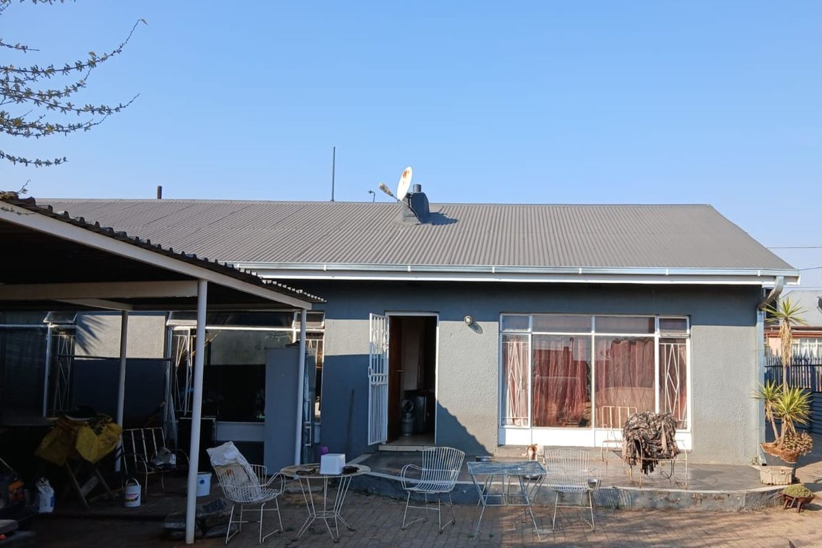 Rear view of the property featuring a paved patio area, corrugated metal roof, and a covered carport structure.