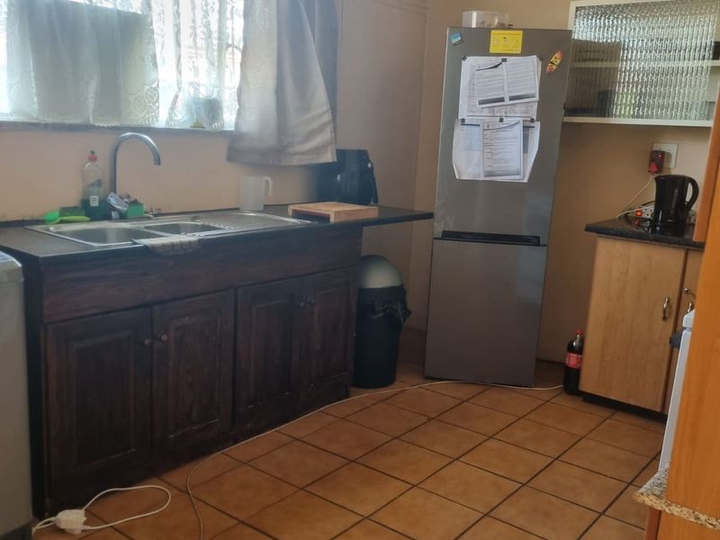 A functional kitchen featuring dark wood cabinetry, double bowl sink, tiled flooring, and ample counter space, offering potential for modern updates.