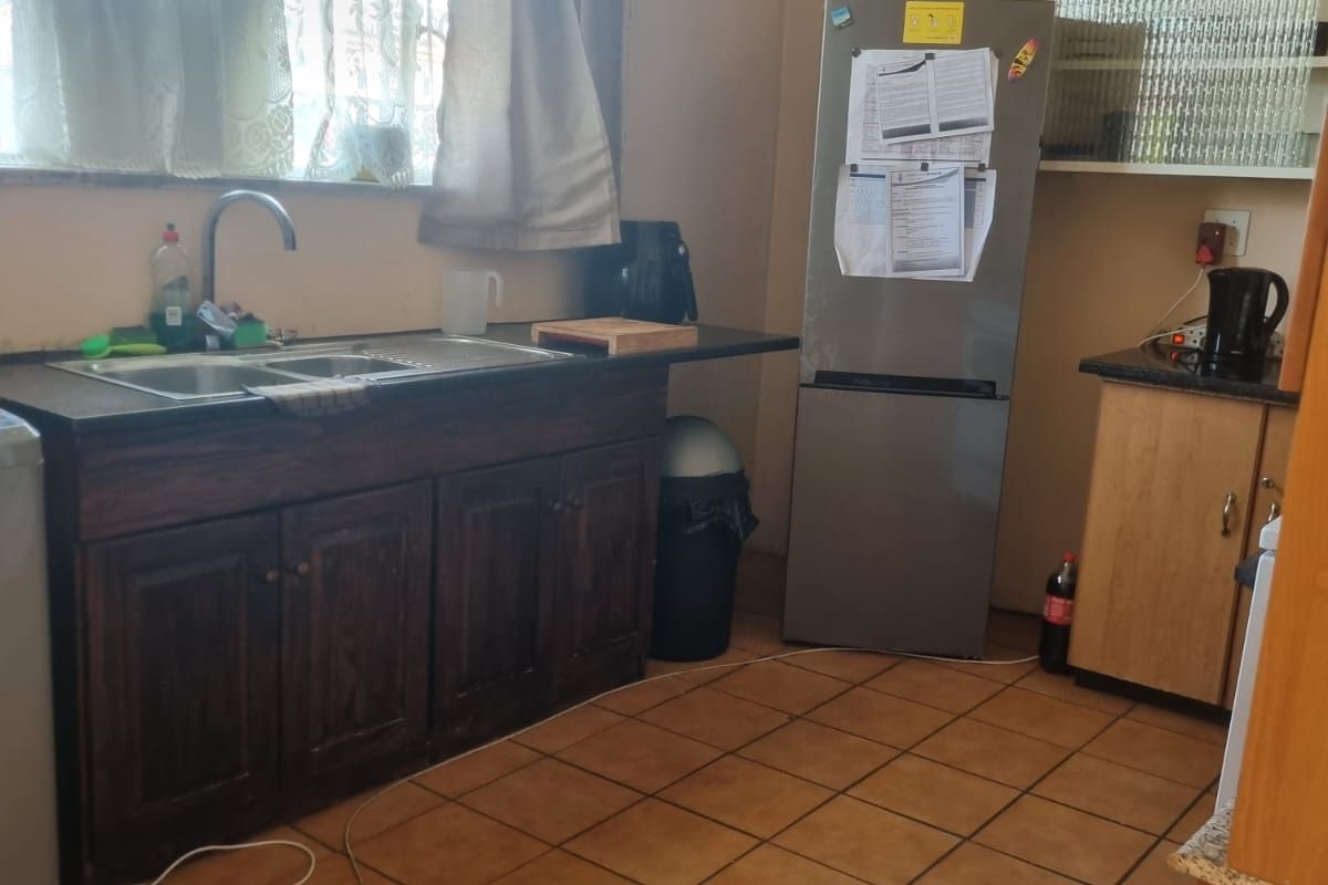 A functional kitchen featuring dark wood cabinetry, double bowl sink, tiled flooring, and ample counter space, offering potential for modern updates.