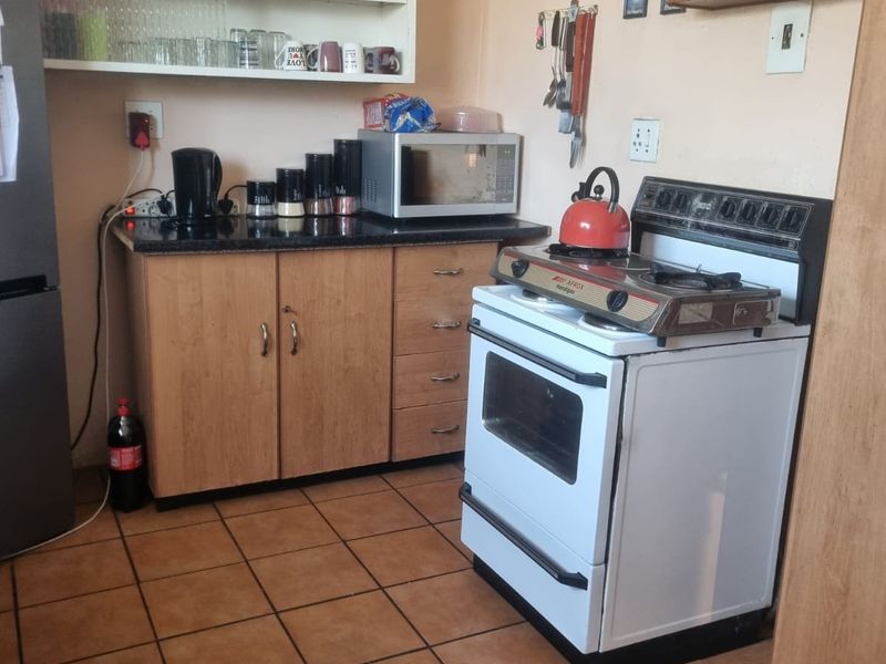 A functional kitchen featuring laminate cabinetry, granite countertops, a freestanding stove, and tiled flooring with open shelving for storage.