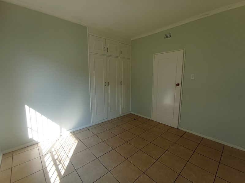 A clean, empty bedroom featuring neutral wall paint, tiled flooring, and built-in storage cupboards.