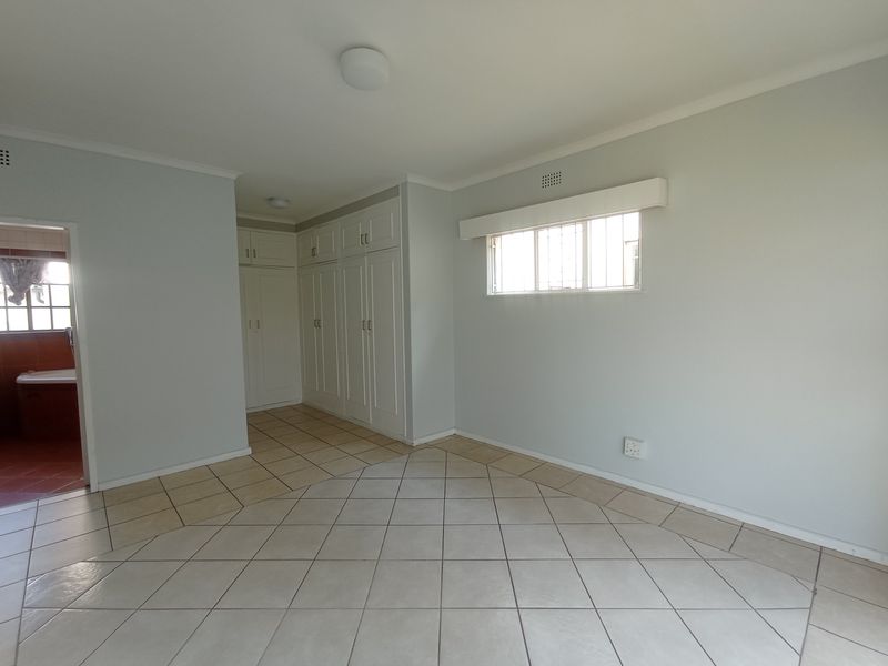 A spacious, empty bedroom featuring neutral tiled flooring, extensive built-in cabinetry, and an adjoining bathroom, offering a clean and versatile living space.