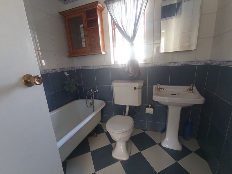 A traditional bathroom featuring a classic clawfoot bathtub, pedestal sink, and blue and white checkered floor tiling with matching wall accents.