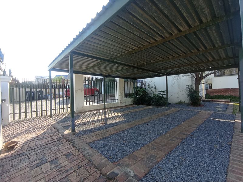 A functional outdoor carport featuring a metal roof structure, gravel parking area with brick edging, and secure metal perimeter fencing.