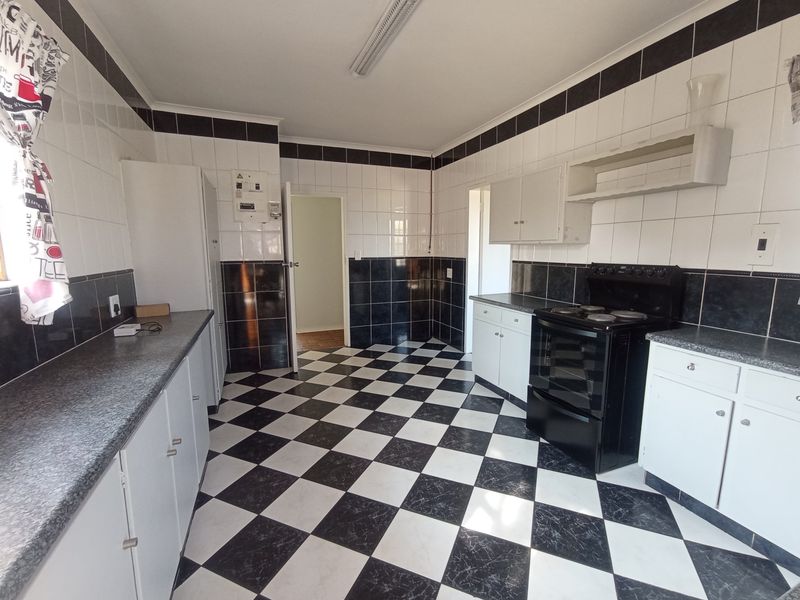 A functional kitchen featuring a classic black and white checkerboard tile theme, built-in cabinetry, and a freestanding electric stove.