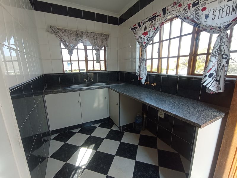 A functional scullery or utility area featuring built-in cabinetry, a stainless steel sink, granite-look countertops, and classic black and white checkerboard floor tiling.