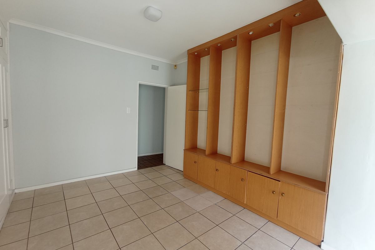 An empty living area featuring neutral tiled flooring and extensive built-in wooden cabinetry with integrated shelving and storage.