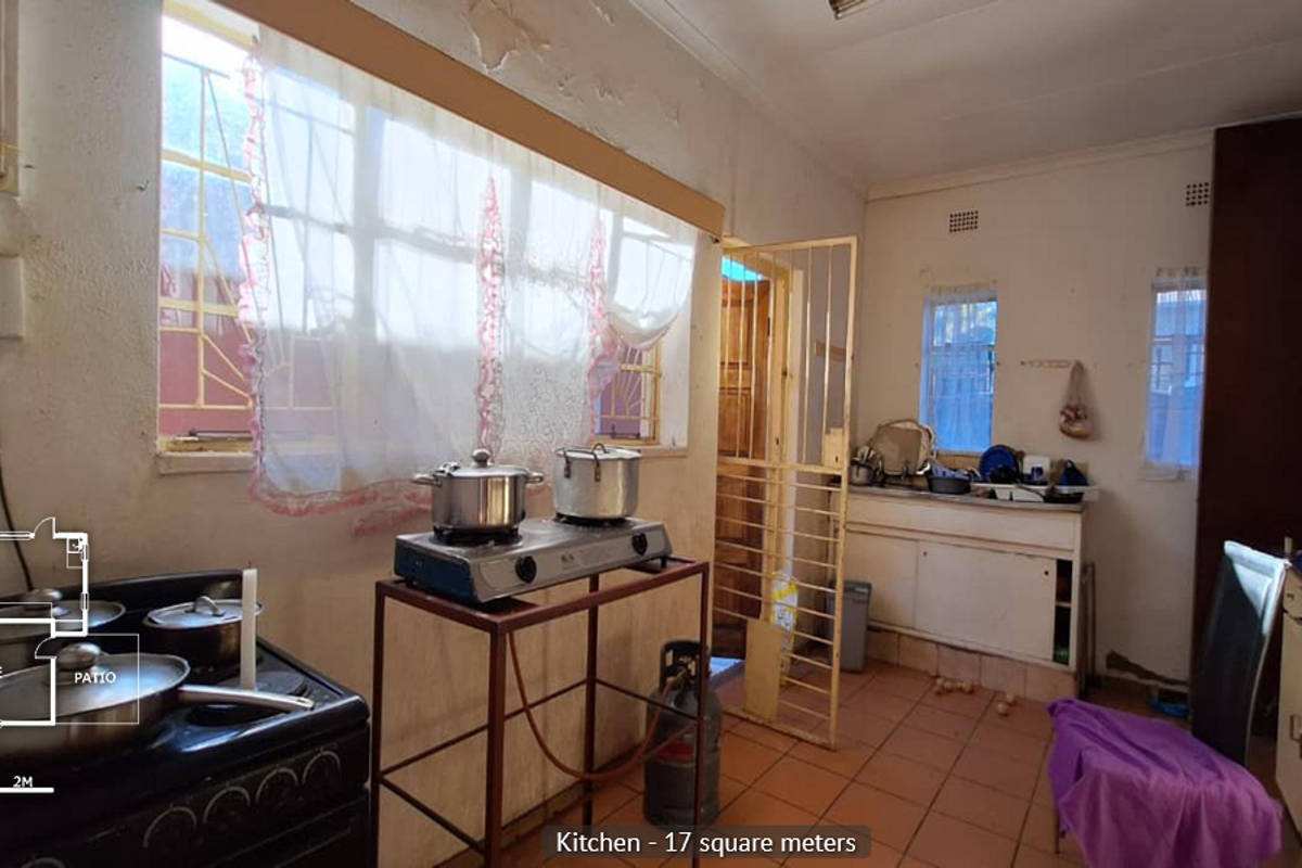 A dated kitchen featuring tiled flooring, built-in cabinetry, and security bars on windows, requiring significant cosmetic updates and repairs to wall finishes.