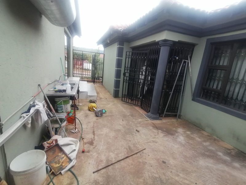 Rear exterior area featuring concrete paving, security gates, and an external sink installation against the side wall of the house.