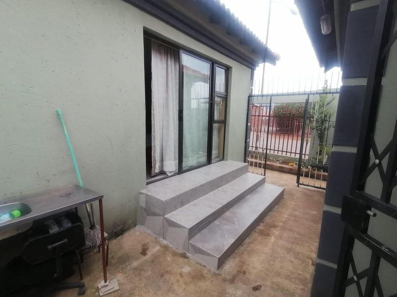 Rear exterior view featuring a sliding glass door entrance with tiled steps and a metal security gate.