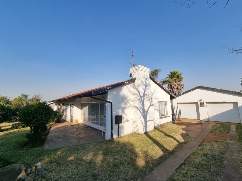 Rear view of the property featuring a stone patio, brick chimney, and a detached double garage with a tiled roof.