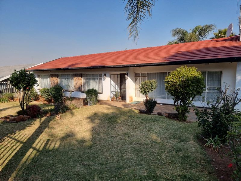 Rear view of a single-story house featuring a tiled roof, paved patio area, and established garden.