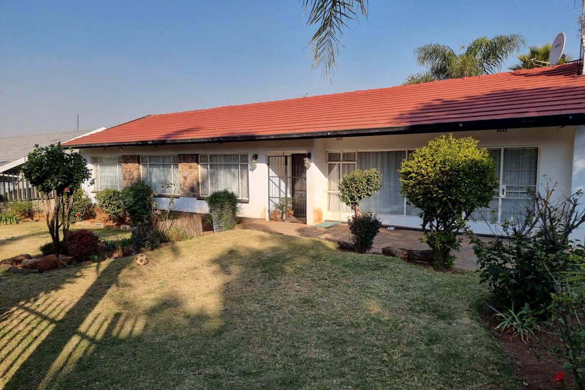 Rear view of a single-story house featuring a tiled roof, paved patio area, and established garden.