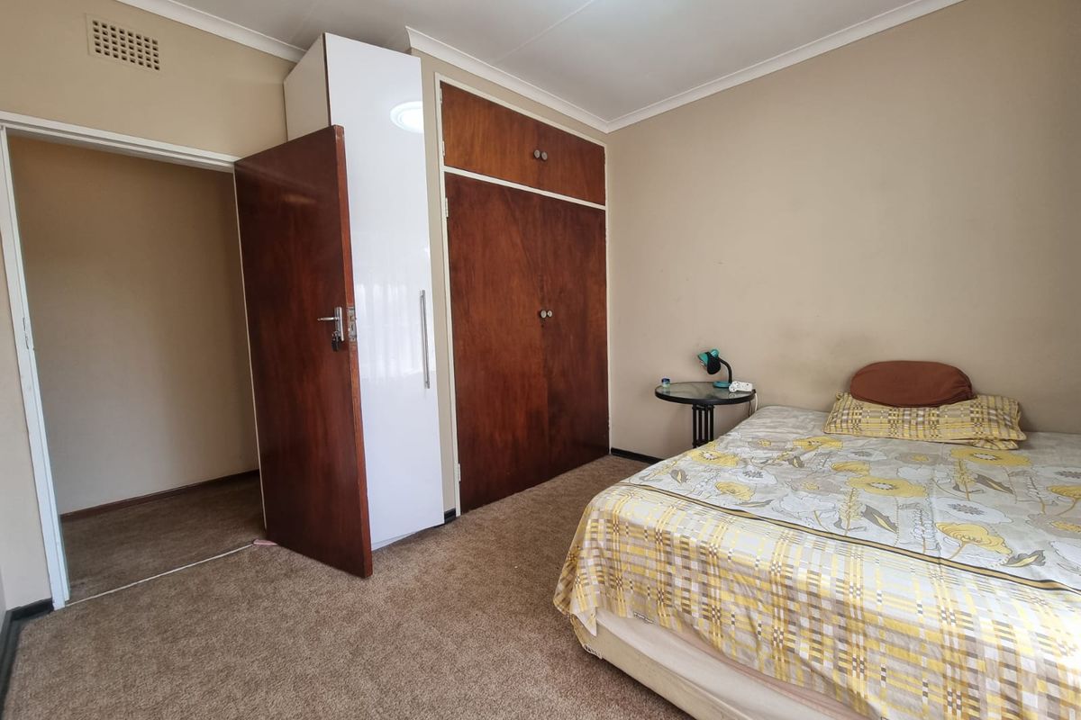 A bedroom featuring built-in wooden cupboards, carpeted flooring, and neutral wall tones, offering a functional space with potential for cosmetic updates.