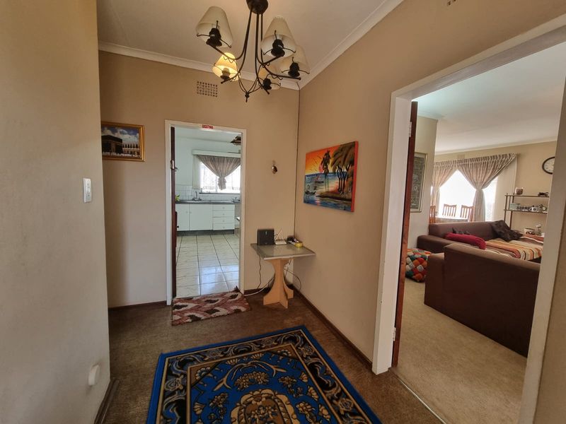 A central hallway providing access to the kitchen and living area, featuring carpeted flooring and a traditional chandelier light fixture.