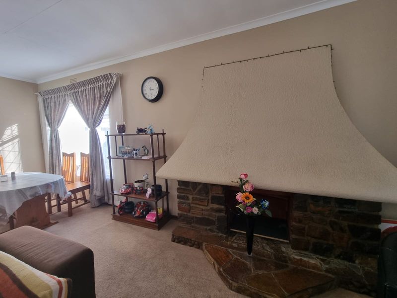 A living room featuring a prominent stone fireplace with a textured hood and stone hearth, complemented by neutral wall finishes and window treatments.