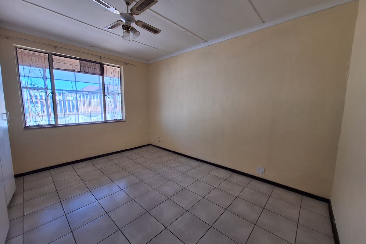An empty bedroom featuring tiled flooring, a ceiling fan, and security bars on the window, providing a blank canvas for potential updates.
