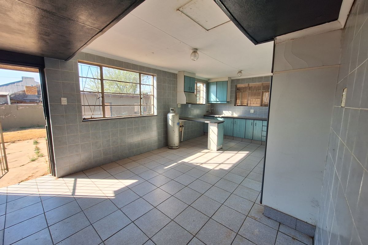 A spacious, empty kitchen featuring tiled walls and floors, built-in cabinetry, and large windows with security bars, offering significant potential for modernization.