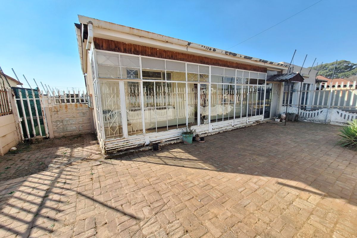 Rear exterior view featuring a large enclosed patio area with paved courtyard, perimeter wall, and electric security fencing.