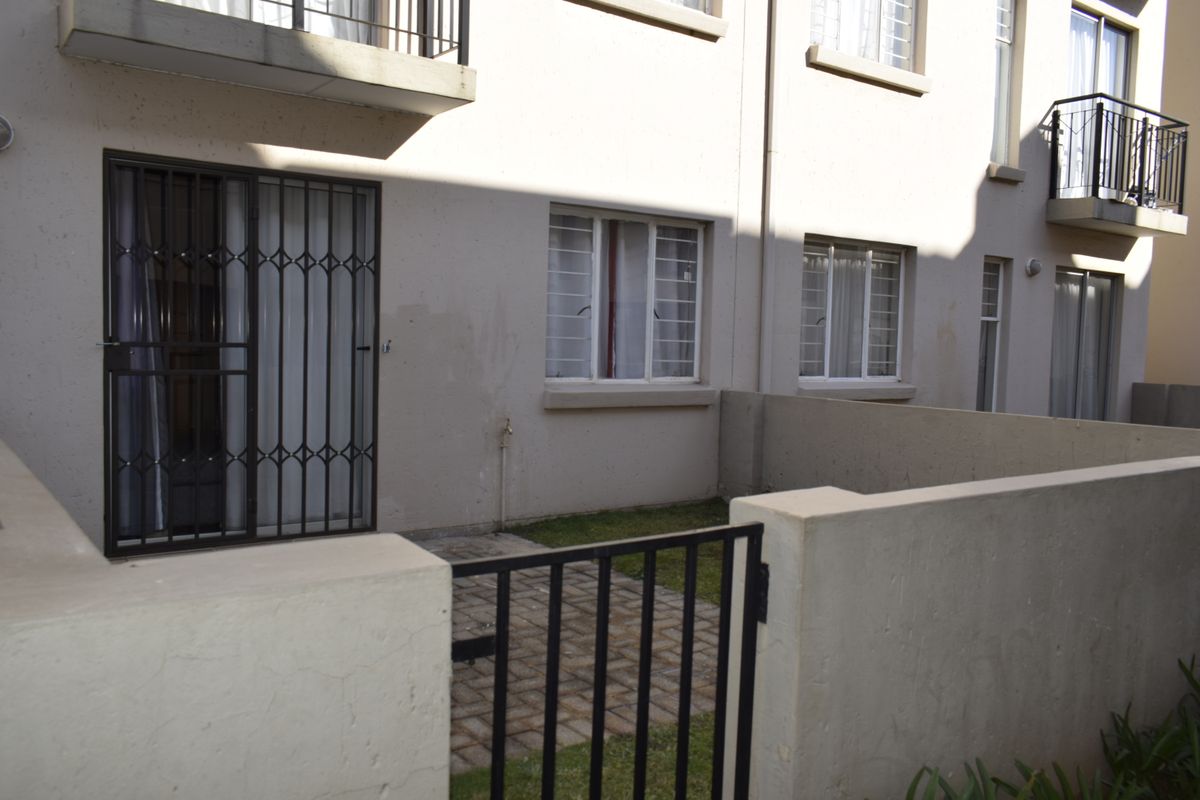Rear exterior view of the townhouse featuring a small paved patio, security gates, and boundary walls with upper-level balconies.