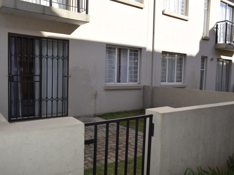 Rear exterior view of the townhouse featuring a small paved patio, security gates, and boundary walls with upper-level balconies.