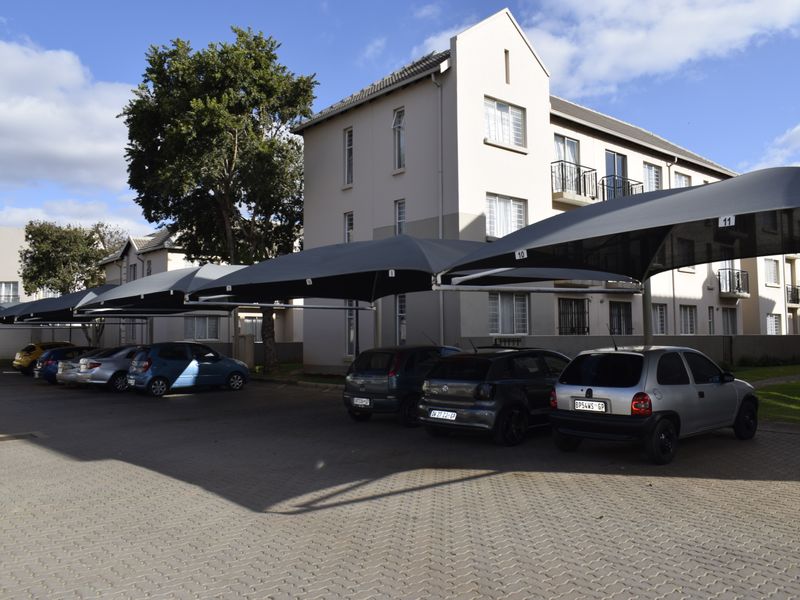 Exterior view of a townhouse complex featuring a paved driveway with designated shade cloth carports and multi-story residential building facades.