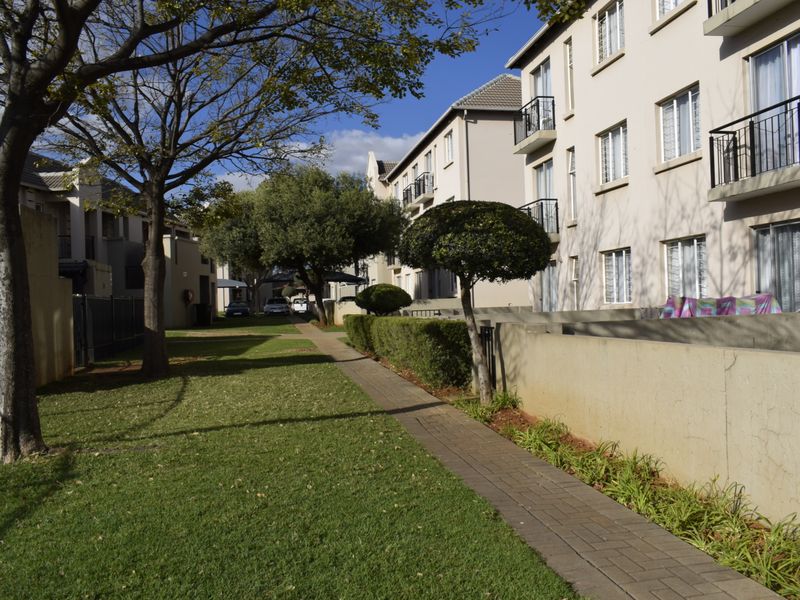 View of the townhouse complex rear exterior featuring a paved walkway, landscaped garden areas, and multi-story residential units with balcony access.
