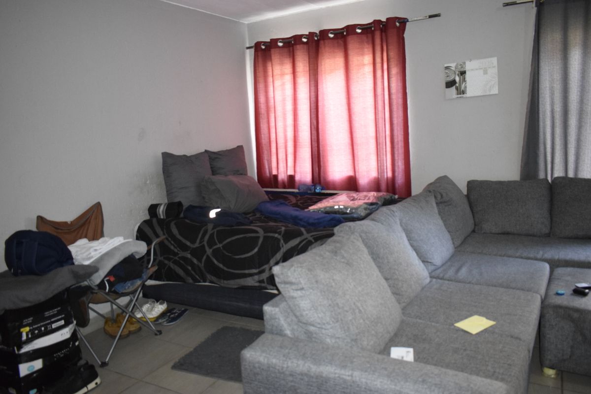 A living room area featuring tiled flooring and a window with a curtain rod, currently showing signs of wear on the wall surfaces.