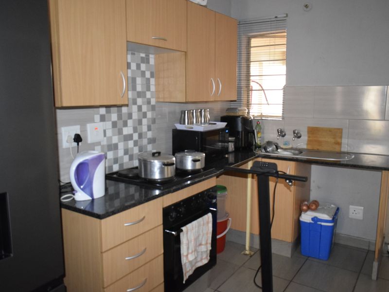 Compact kitchen featuring laminate cabinetry, granite countertops, mosaic tile backsplash, built-in oven, and electric hob with tiled flooring.