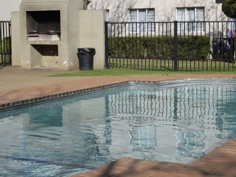 Outdoor pool area featuring a swimming pool with brick coping, a built-in braai structure, and metal perimeter fencing.