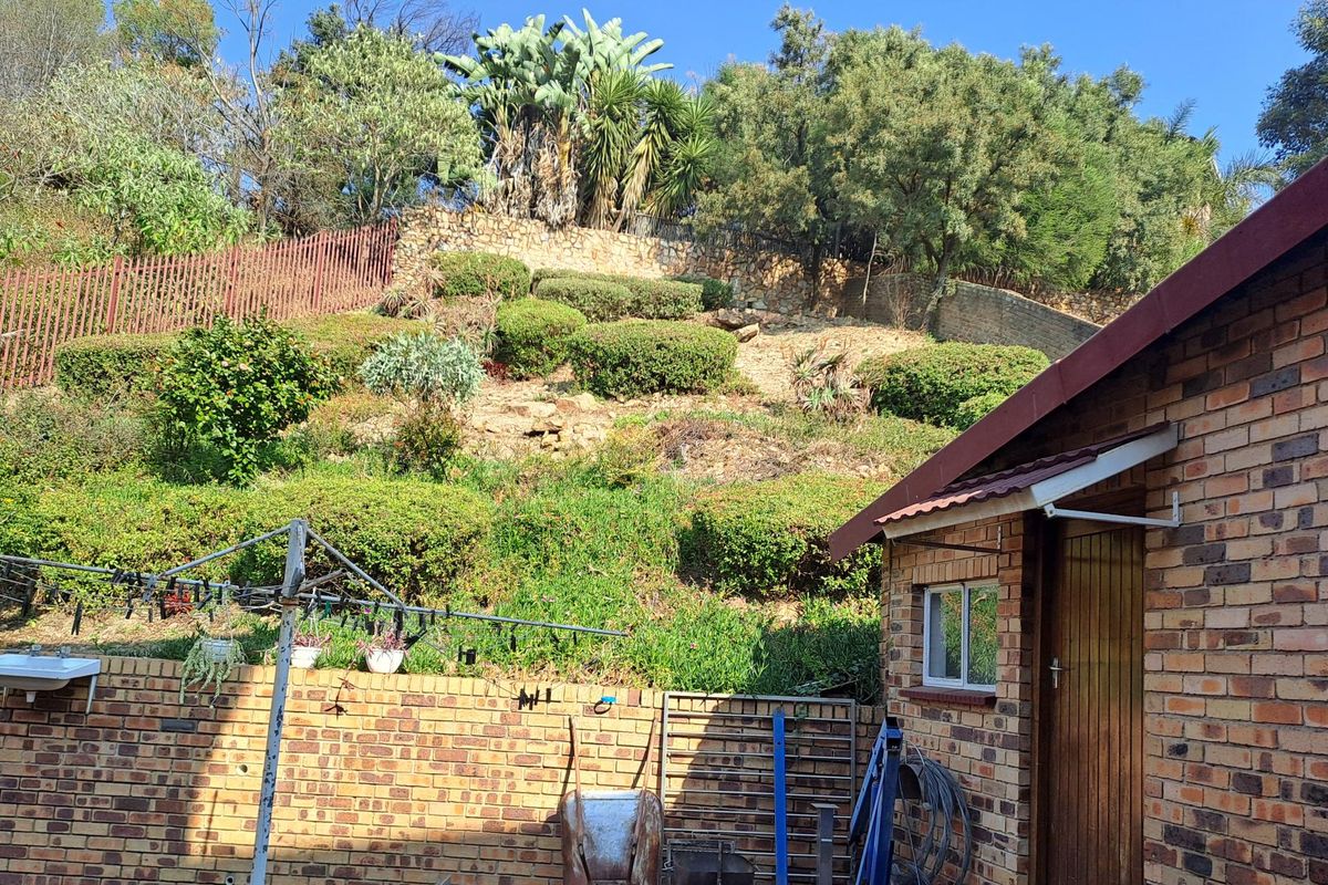 Rear exterior view featuring a face brick structure, an external wash basin, and a terraced garden with established landscaping and retaining walls.