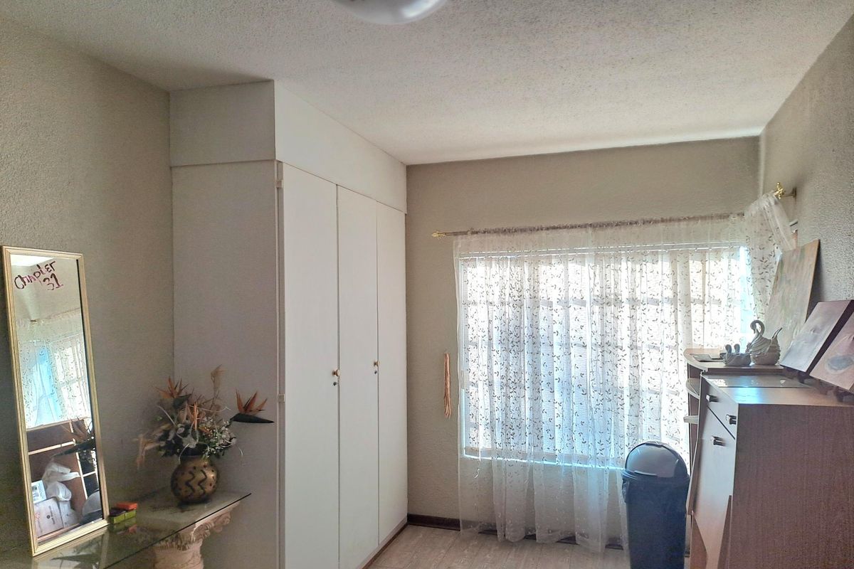 A bedroom featuring built-in wardrobes, laminate flooring, and a textured ceiling, offering a functional space with natural light.