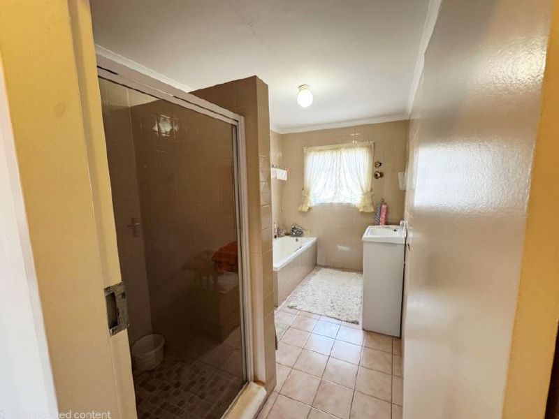 A functional bathroom featuring a shower enclosure, built-in bathtub, and pedestal basin with neutral tiled finishes throughout.