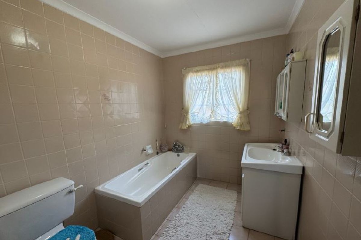A functional bathroom featuring a built-in bathtub, vanity basin, and full-height wall tiling, offering potential for a modern renovation.