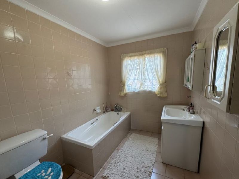 A functional bathroom featuring a built-in bathtub, vanity basin, and full-height wall tiling, offering potential for a modern renovation.