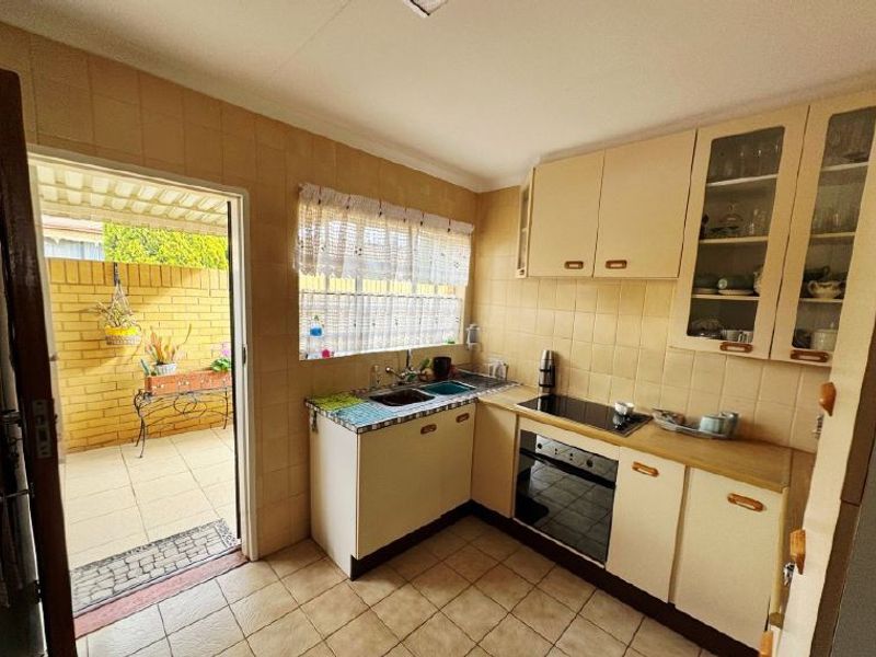 A compact, dated kitchen featuring built-in cabinetry, an electric hob, and oven, with direct access to an outdoor patio area.