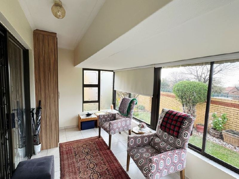A bright, enclosed patio area featuring tiled flooring, built-in cabinetry, and large windows overlooking the garden, offering a versatile space for relaxation.