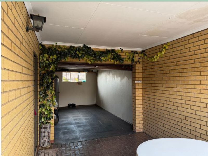 A covered garage area featuring exposed brick walls, paved flooring, and a wall-mounted light fixture, showing signs of damp on the interior wall.