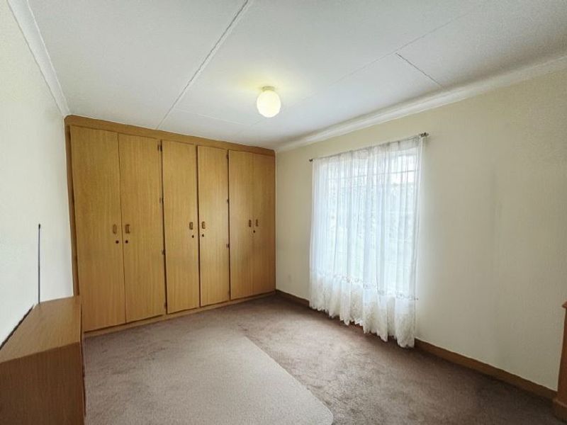 A spacious bedroom featuring extensive built-in wooden cupboards, neutral wall finishes, and carpeted flooring, offering a blank canvas for personalization.