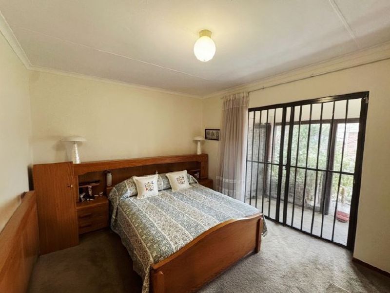 A bedroom featuring a built-in wooden headboard with integrated bedside tables, carpeted flooring, and a sliding glass door with a security gate leading outside.
