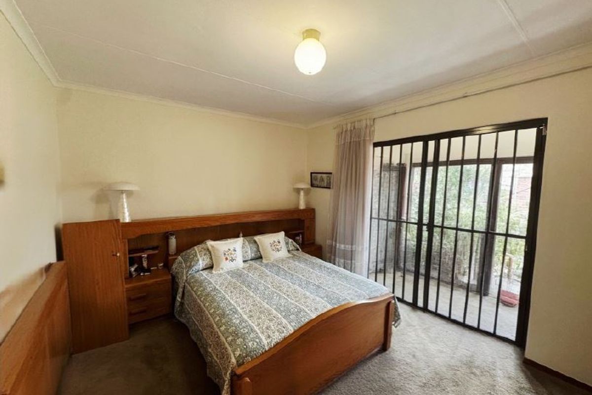 A bedroom featuring a built-in wooden headboard with integrated bedside tables, carpeted flooring, and a sliding glass door with a security gate leading outside.