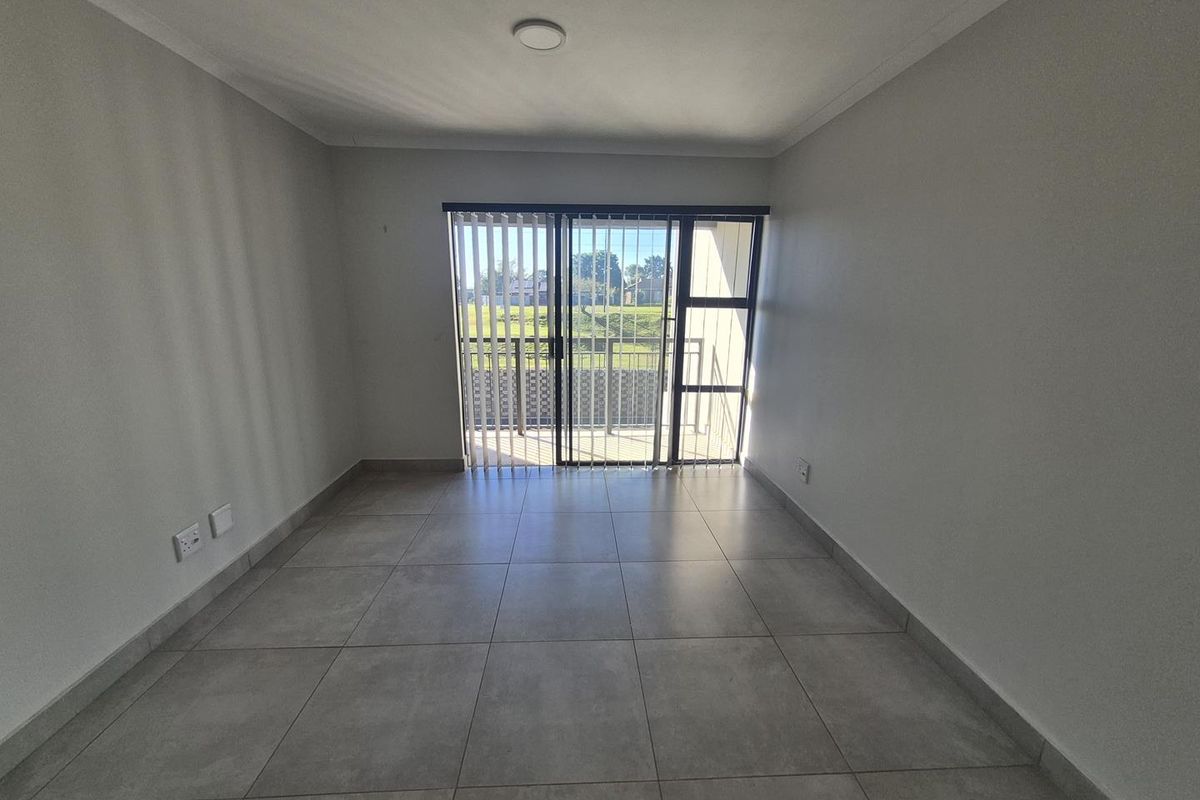 An empty living room featuring large format floor tiles, neutral walls, and a sliding glass door providing access to a balcony.