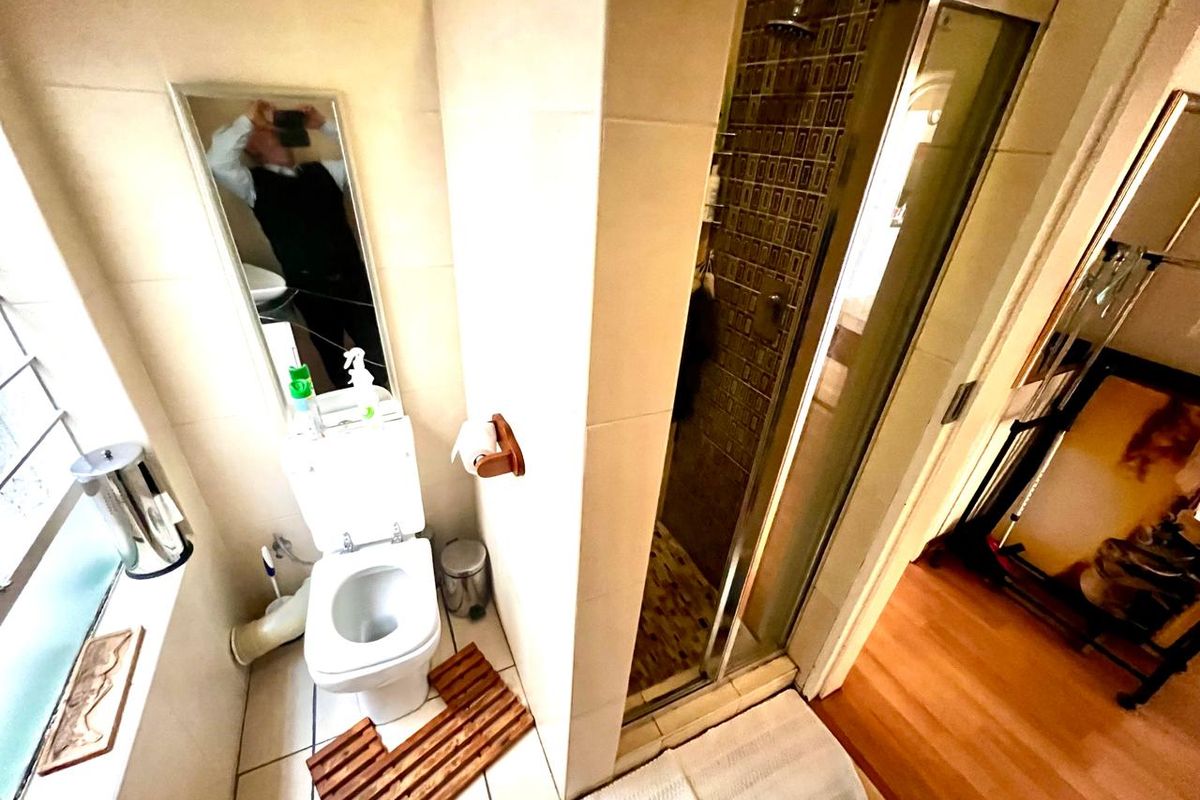A compact bathroom featuring a tiled shower enclosure, a standard toilet, and wall-mounted mirror, providing essential functional amenities in a small footprint.