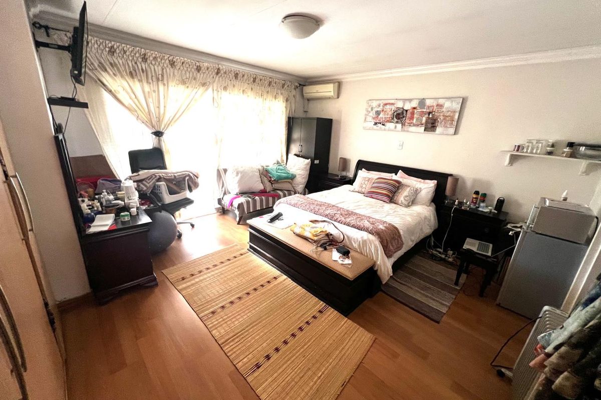 A bedroom featuring laminate flooring, a split-system air conditioner, and sliding glass doors providing natural light.