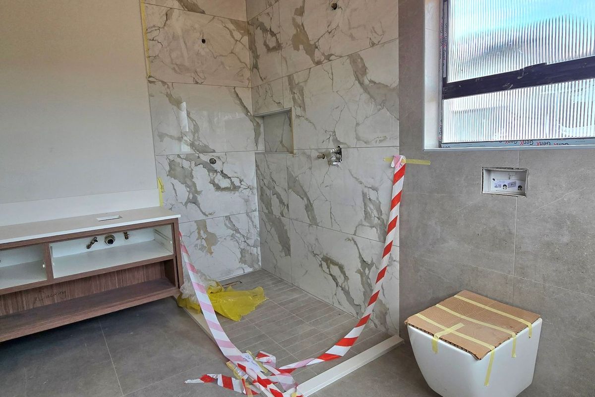 A bathroom under construction featuring marble-look wall tiles, a floating vanity unit, and a wall-mounted toilet, currently awaiting final plumbing and finishing touches.