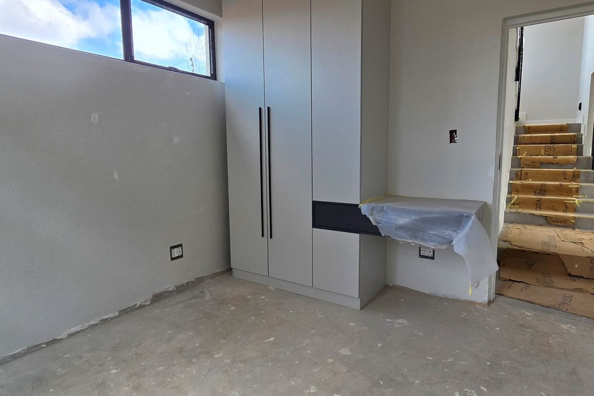 A bedroom or study area under construction, featuring built-in cabinetry, a desk unit, and access to a staircase with protective floor coverings.